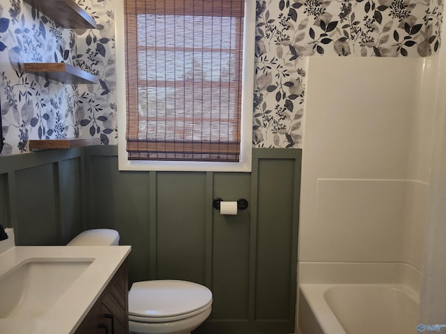 bathroom featuring toilet, wallpapered walls, a tub to relax in, and a wainscoted wall