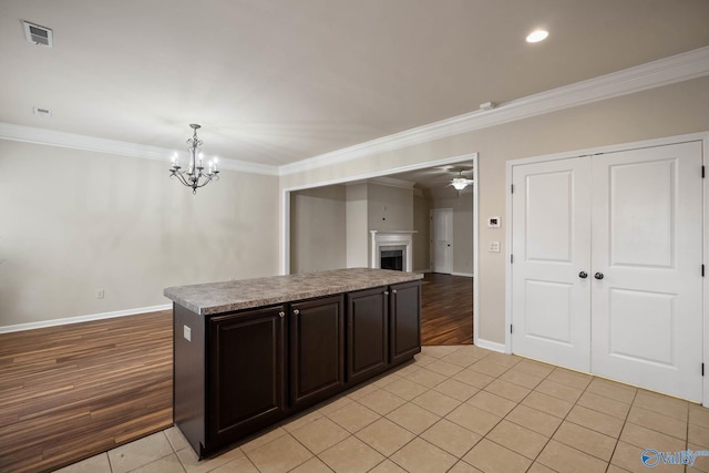 kitchen featuring a fireplace, light tile patterned floors, visible vents, ornamental molding, and ceiling fan with notable chandelier