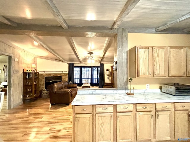 kitchen featuring light wood-style floors, light brown cabinets, beam ceiling, and a stone fireplace