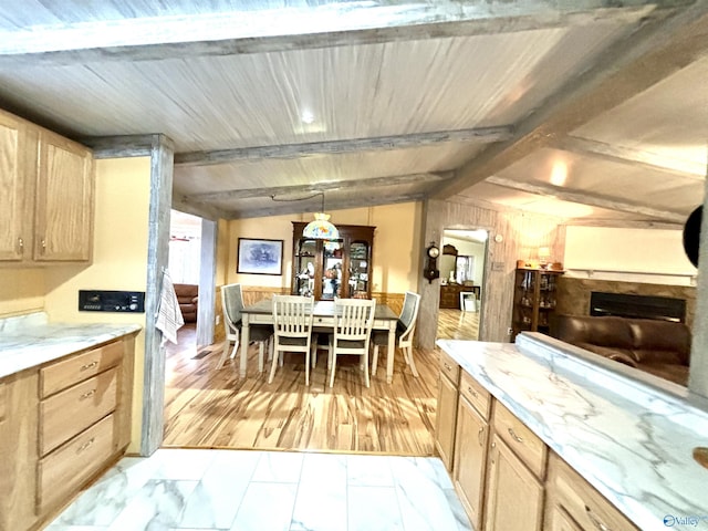 kitchen featuring vaulted ceiling with beams, light stone counters, light brown cabinets, a fireplace, and pendant lighting