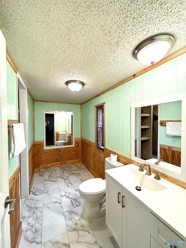 bathroom with toilet, marble finish floor, crown molding, and wainscoting