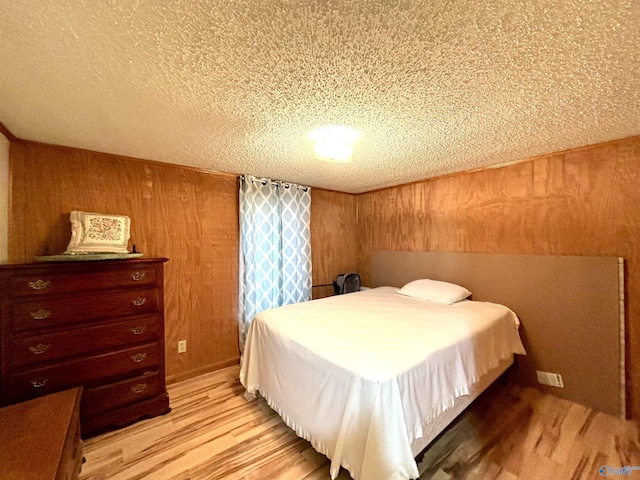 bedroom with wooden walls, light wood finished floors, and a textured ceiling