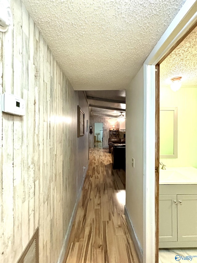 hallway with a textured ceiling, wooden walls, wood finished floors, a sink, and baseboards