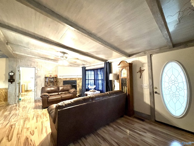 living room featuring a ceiling fan, a wall unit AC, wood finished floors, a fireplace, and beam ceiling