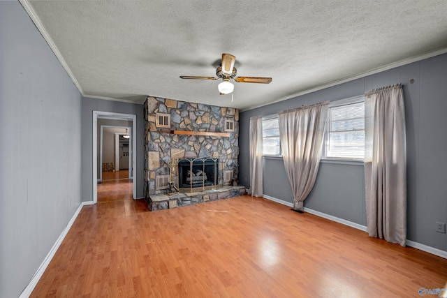 unfurnished living room with hardwood / wood-style flooring, ceiling fan, a stone fireplace, and a textured ceiling