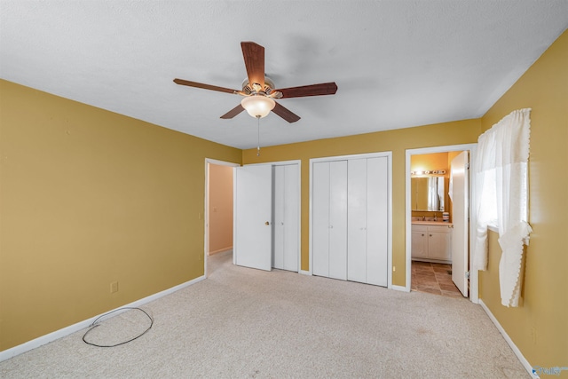 unfurnished bedroom featuring ensuite bathroom, ceiling fan, light carpet, and multiple closets