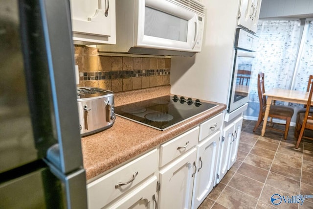 kitchen with electric cooktop, oven, backsplash, white cabinetry, and stainless steel fridge