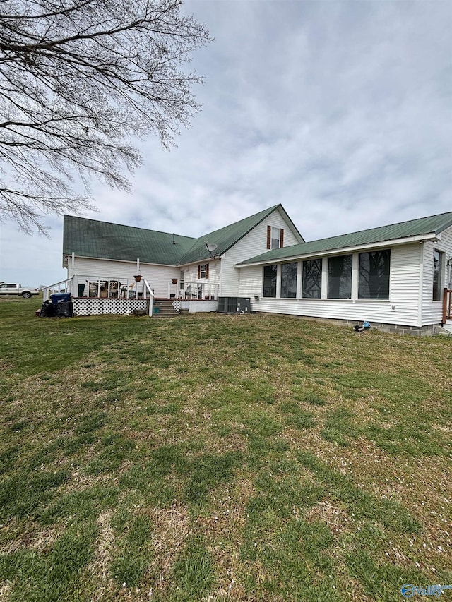 back of house featuring a sunroom, central air condition unit, a wooden deck, metal roof, and a lawn