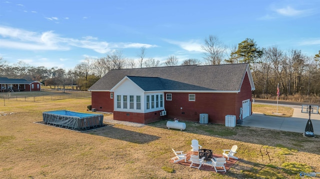 rear view of house with a fire pit, a garage, central air condition unit, and a lawn