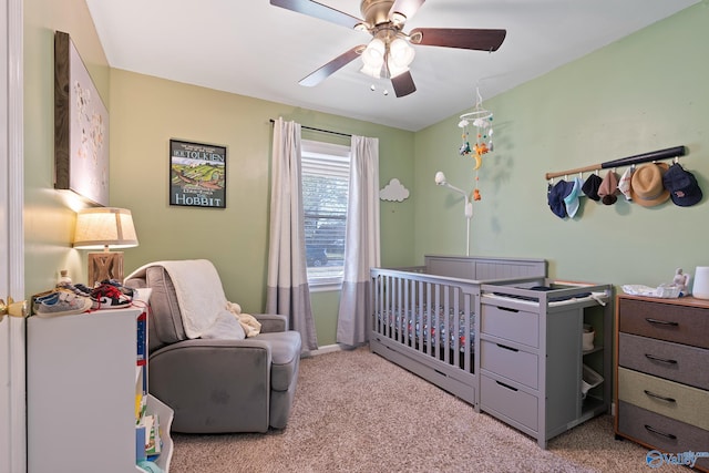 bedroom featuring ceiling fan, a nursery area, and light carpet