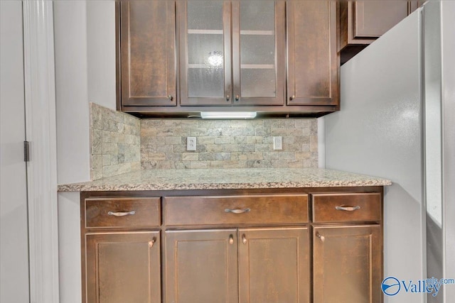 kitchen featuring glass insert cabinets, freestanding refrigerator, light stone countertops, and tasteful backsplash