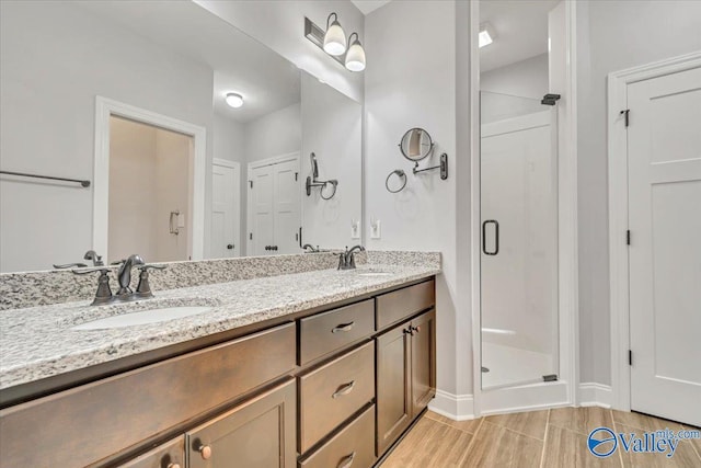 full bath featuring baseboards, double vanity, a sink, and a shower stall