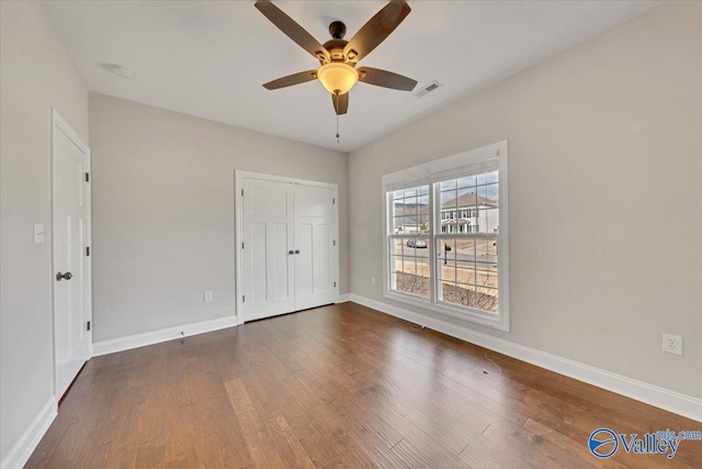 unfurnished bedroom with dark wood-style floors, baseboards, visible vents, and a closet