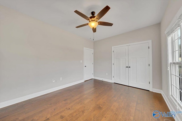 unfurnished bedroom with dark wood-type flooring, a closet, a ceiling fan, and baseboards