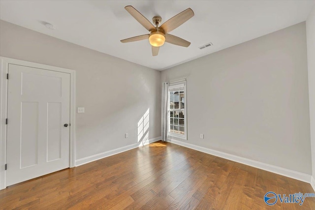 spare room with wood finished floors, visible vents, and baseboards