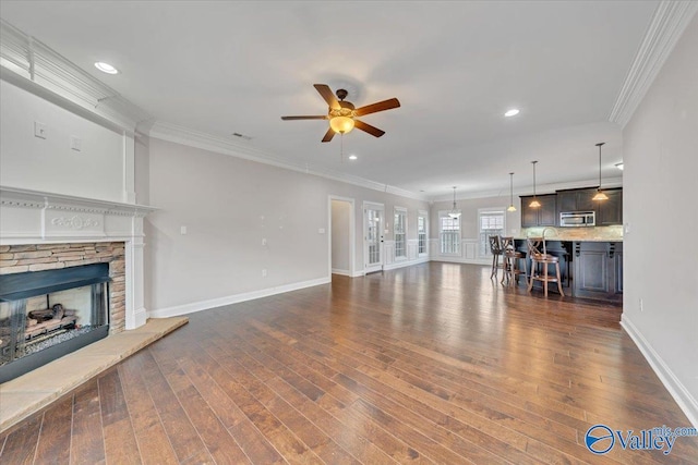 unfurnished living room featuring crown molding, baseboards, dark wood-style flooring, and a stone fireplace