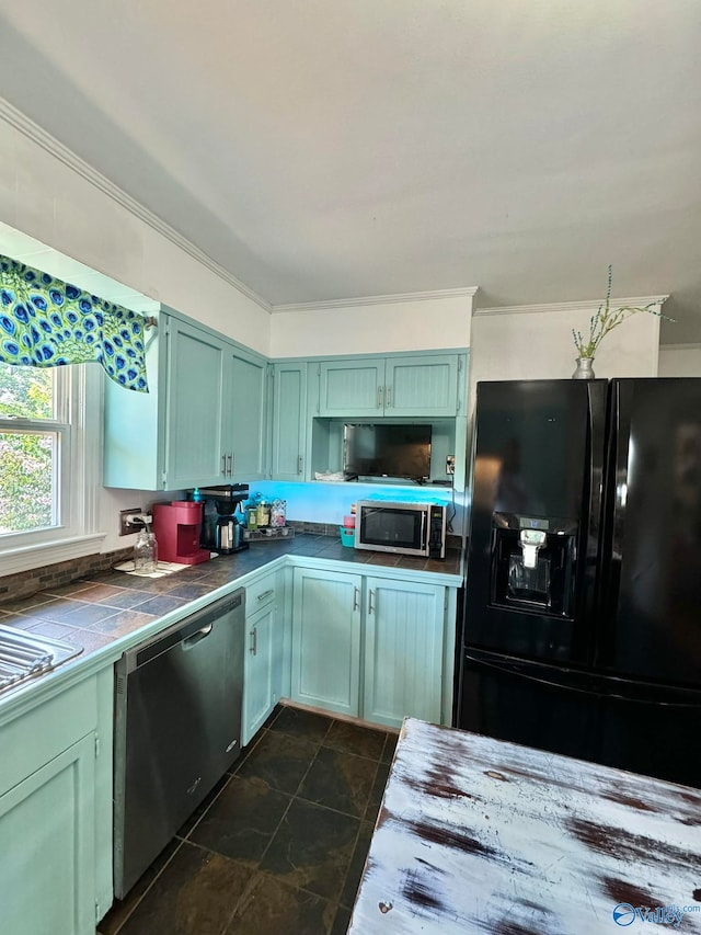 kitchen with appliances with stainless steel finishes, ornamental molding, dark tile patterned flooring, green cabinets, and tile counters