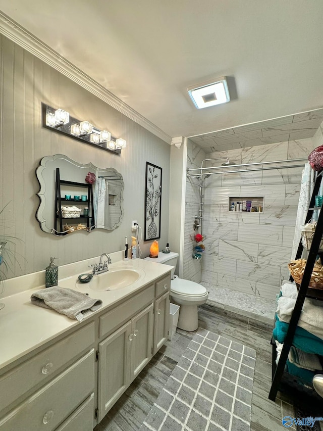 bathroom with tiled shower, crown molding, toilet, and vanity