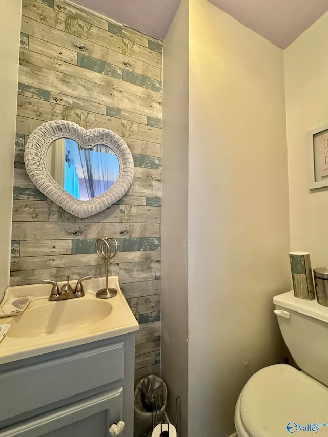 bathroom with toilet, wooden walls, and vanity