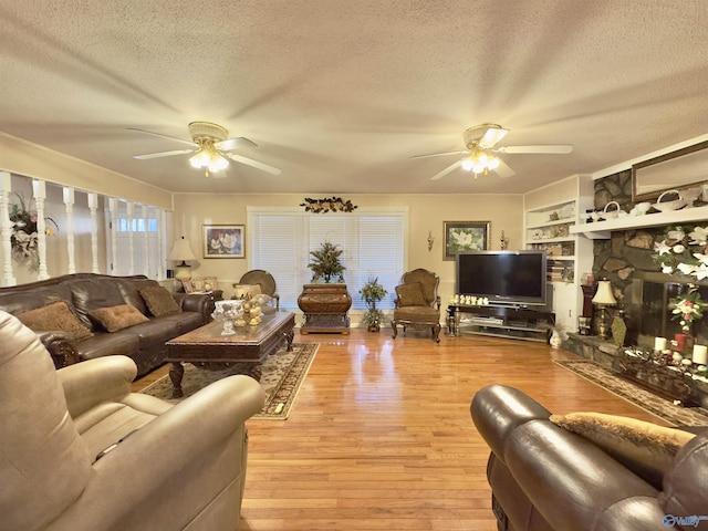 living room with a stone fireplace, ceiling fan, a textured ceiling, and light wood-type flooring