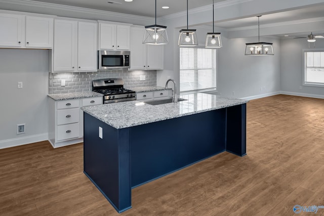 kitchen with a center island with sink, white cabinets, hanging light fixtures, stainless steel appliances, and a sink