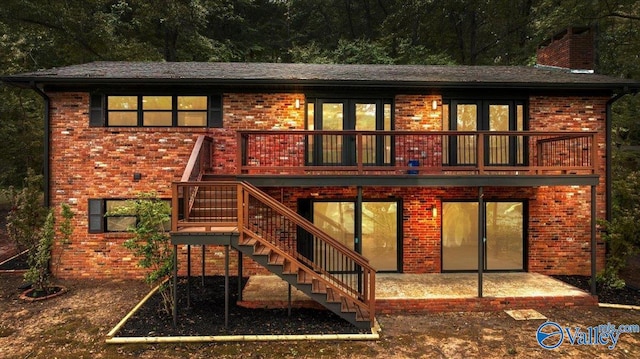 rear view of house featuring brick siding, stairs, a wooden deck, a chimney, and a patio area