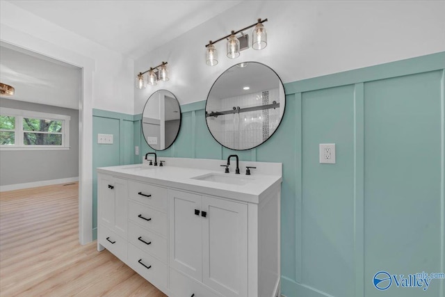 full bathroom with double vanity, wood finished floors, tiled shower, and a sink