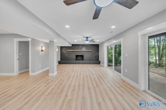 unfurnished living room featuring baseboards, plenty of natural light, light wood-style flooring, and a brick fireplace