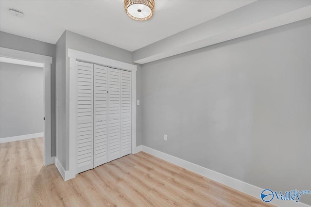 unfurnished bedroom featuring light wood finished floors, baseboards, and a closet