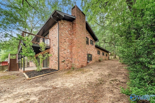 view of home's exterior with stairs, a chimney, a deck, and brick siding