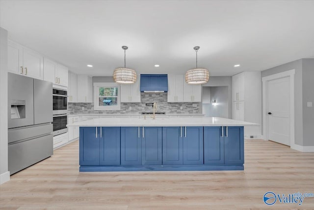 kitchen with light countertops, hanging light fixtures, wall chimney range hood, and stainless steel appliances