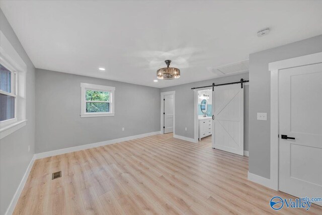 unfurnished bedroom featuring visible vents, light wood-style flooring, a barn door, connected bathroom, and baseboards