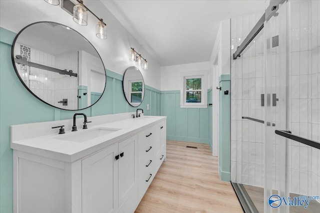 full bathroom with double vanity, a wainscoted wall, a sink, and wood finished floors