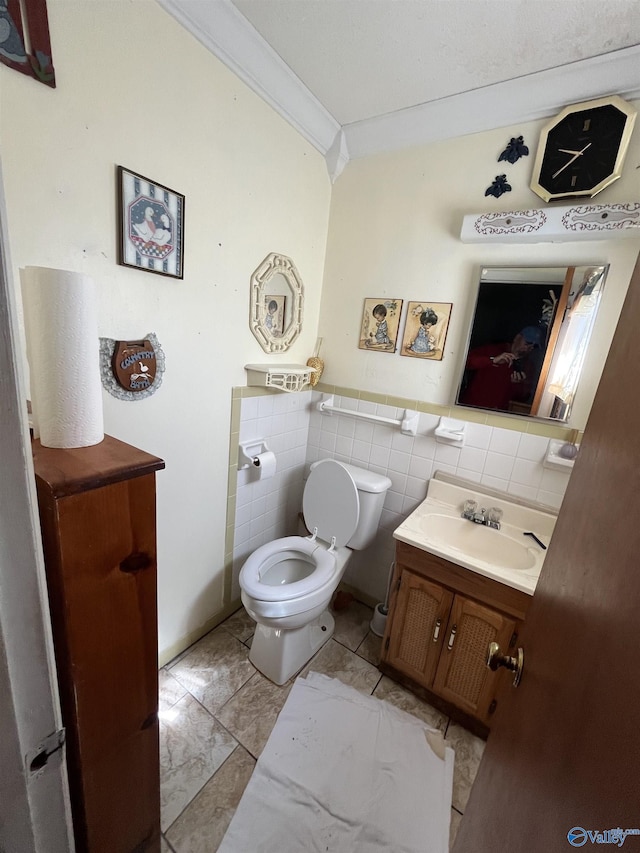 half bath featuring toilet, ornamental molding, tile walls, wainscoting, and vanity