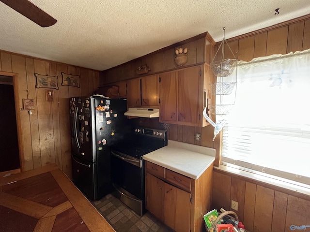 kitchen with under cabinet range hood, freestanding refrigerator, wood walls, light countertops, and stainless steel electric range oven