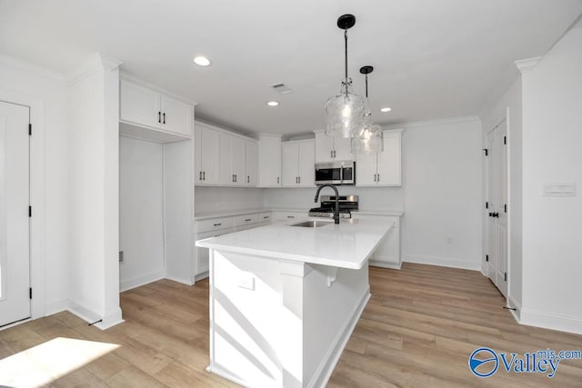 kitchen with decorative light fixtures, an island with sink, sink, white cabinets, and stainless steel appliances