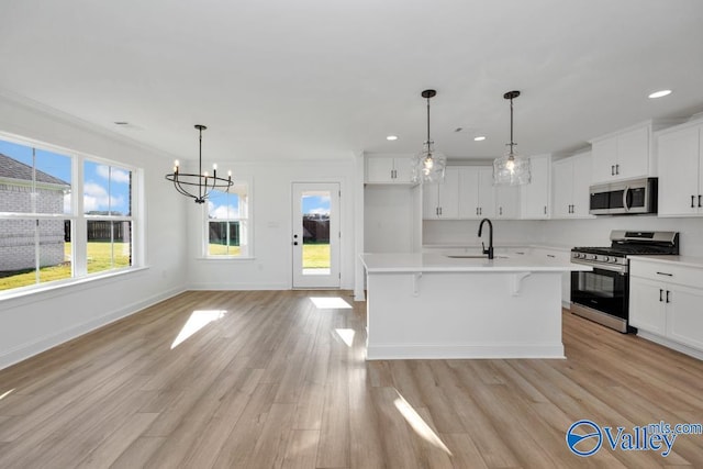 kitchen with white cabinetry, appliances with stainless steel finishes, decorative light fixtures, and a center island with sink