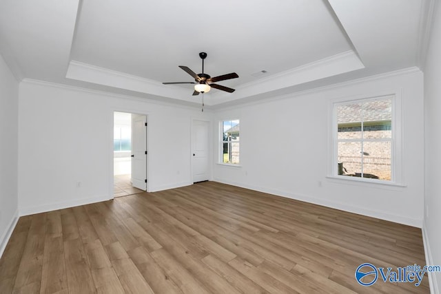 empty room with a raised ceiling, crown molding, ceiling fan, and light hardwood / wood-style floors