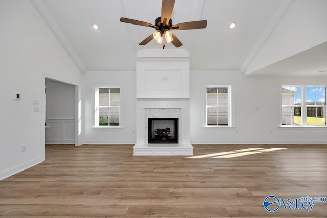 unfurnished living room with ceiling fan, high vaulted ceiling, a high end fireplace, and light hardwood / wood-style flooring