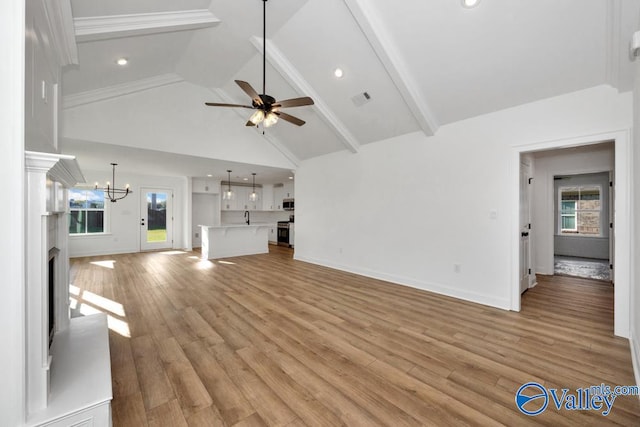 unfurnished living room with ceiling fan with notable chandelier, high vaulted ceiling, sink, light hardwood / wood-style floors, and beam ceiling