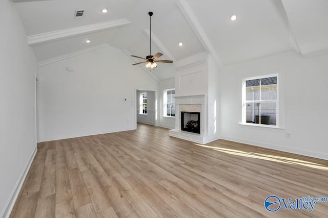 unfurnished living room featuring a wealth of natural light, a premium fireplace, beamed ceiling, and light wood-type flooring