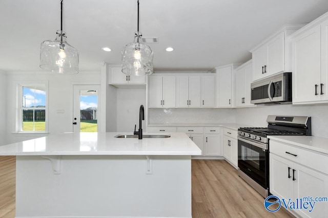 kitchen with appliances with stainless steel finishes, pendant lighting, white cabinetry, sink, and a kitchen island with sink