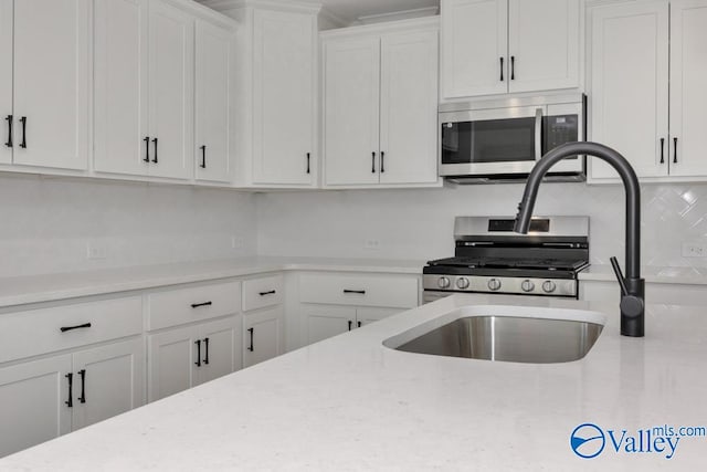 kitchen featuring white cabinetry, stainless steel appliances, light stone countertops, and decorative backsplash