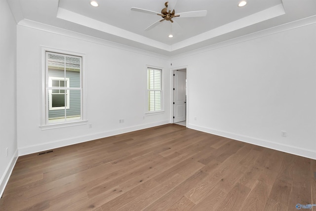 empty room with ceiling fan, wood-type flooring, ornamental molding, and a tray ceiling