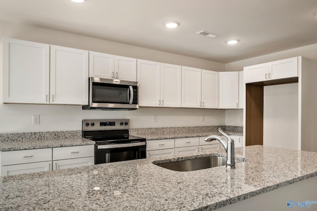 kitchen featuring visible vents, a sink, white cabinetry, stainless steel appliances, and light stone countertops