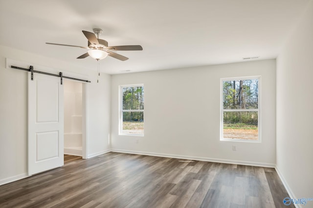 unfurnished bedroom featuring multiple windows, dark wood-type flooring, and a barn door