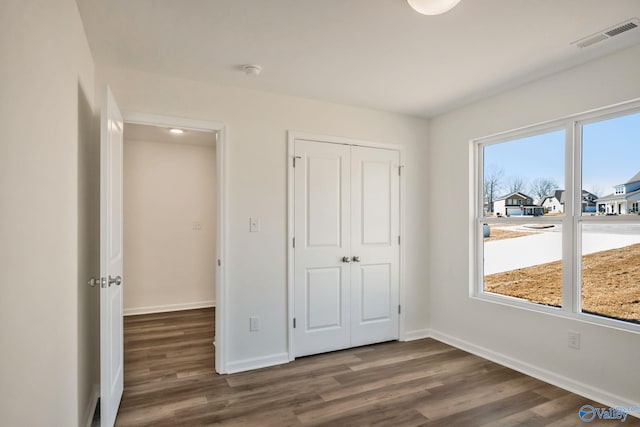 unfurnished bedroom featuring visible vents, baseboards, a closet, and dark wood-style flooring