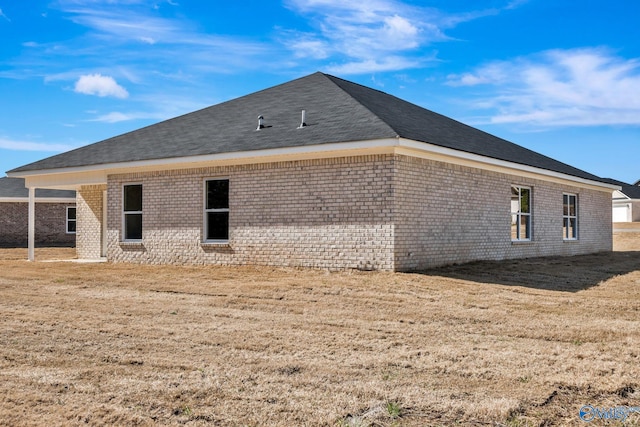 back of property with a yard, brick siding, and a shingled roof