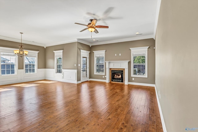 unfurnished living room with hardwood / wood-style flooring, ornamental molding, plenty of natural light, and ceiling fan with notable chandelier