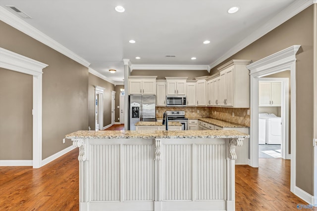 kitchen with appliances with stainless steel finishes, a kitchen breakfast bar, ornamental molding, light stone countertops, and light hardwood / wood-style flooring